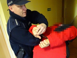 policjant prowadzi zatrzymanego w kajdankach