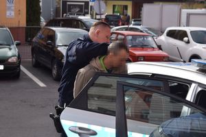 Policjant trzyma zatrzymanego zakutego w kajdanki przy radiowozie