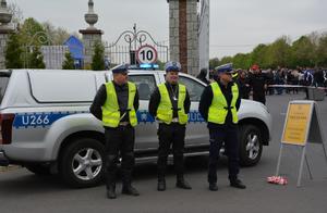 Trzej umundurowani policjanci służby ruchu drogowego stoją na tle oznakowanego radiowozu