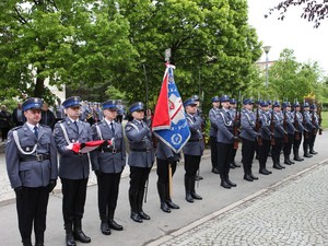 Kompania honorowa stoi przed pomnikiem obok poczet sztandarowy z flag Polski.