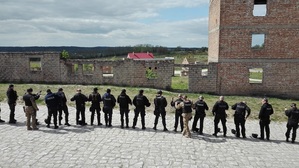 Policjanci uczestnicy szkolenia stoją w szeregu i wkładają broń do kabur lub trzymają ją w ręce