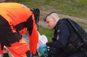 Policjant z Oddziału Prewencji Policji w Poznaniu  pochyla się nad ratowaną osobą, obok ratownik medyczny