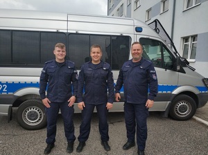 Trzej policjanci z Oddziału Prewencji Policji w Poznaniu stoją na tle oznakowanego radiowozu