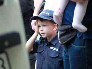 chopiec w policyjnym mundurze stoi trzymajc za rk rodzica