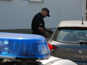 Fragment policyjnego koguta, w tle policjant wręczający ulotkę kierowcy samochodu