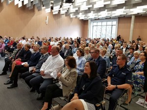 Pełna sala ludzi siedzących w krzesełkach - na przedzie siedzi I Zastępca Komendanta Wojewódzkiego Policji w Poznaniu