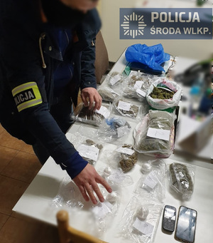 Na zdjęciu widać umundurowanego policjanta z zakrytą twarzą oglądającego zabezpieczone narkotyki i sprzęt do ich produkcji.